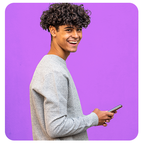 Jovem preto, cabelos cacheados, de perfil, com um moletom cinza, sorrindo, segurando um celular sobre um fundo lilás.