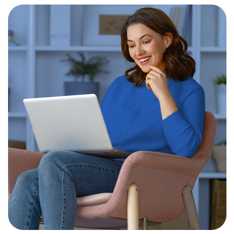 Mulher jovem de blusa azul, sorrindo, olhando o notebook que está no colo, enquanto está sentado em uma poltrona.